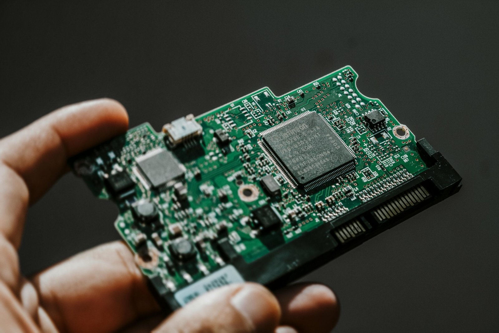Close-up view of a green circuit board held by a hand, showcasing technology details.